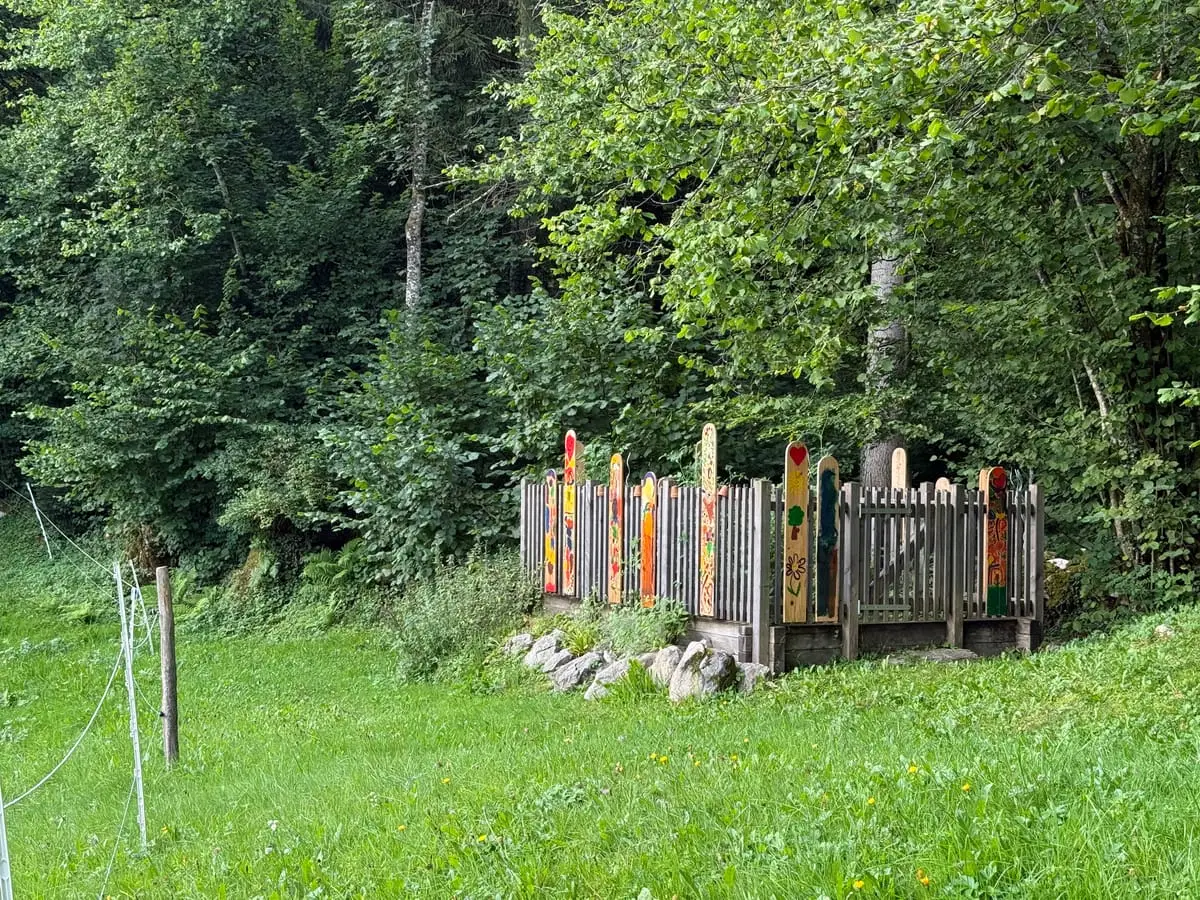Von Kindern bunt bemalte Zaunlatten am Waldrand der Spielwiese.
